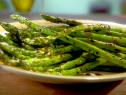 A close up of grilled asparagus on a yellow and white plate. The asparagus is green and has a balsamic drizzle on it. The drizzle is made from balsamic vinegar, lemon zest, lemon juice and salt. The plate is sitting on a dark brown wood surface.