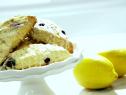 A platter of homemade blueberry scones that have been topped with a drizzle of lemon glaze. Next to the platter are two whole lemons.
