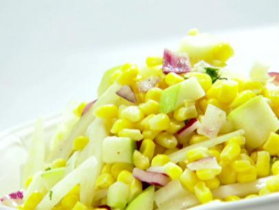 A close up of a corn salad. The salad contains corn, granny smith apples, red onins, fennel and a dressing made from flat leaf parsley, apple cider vinegar, brown mustard, canola oil and cumin. The salad is sitting on a white plate.