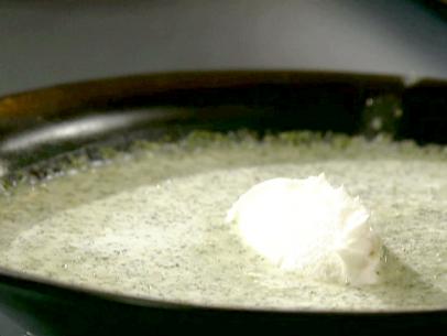 A close up of a broccoli soup. The soup is made from broccoli, chicken stock, shallots, olive oil and mascarpone cheese. There is a dallop of mascarpone cheese sitting on top of the soup. The soup is in a black bowl. The soup is a bright green color.