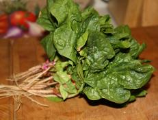 A bunch of Spinach Greens gathered with a red rubberband and placed on a wooden surface