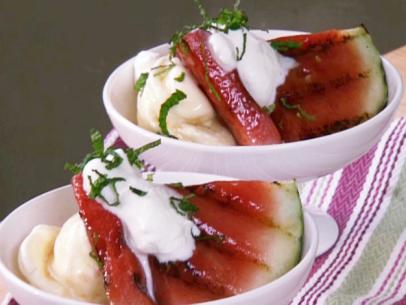 Grilled watermelon sundae has slices of grilled watermelon brushed with a honey and lime syrup served with vanilla ice cream, whipped cream, and a garnish of sliced mint leaves.