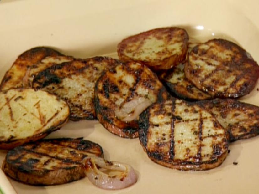 Sliced red potatoes and shallots have been grilled and placed in a casserole dish.