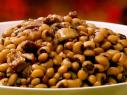 A bowl of black eyed peas are served with bacon and pork.