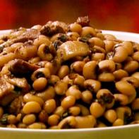 A bowl of black eyed peas are served with bacon and pork.