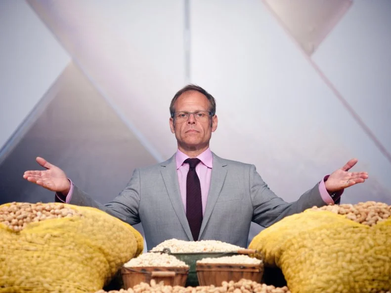 Host Alton Brown revealing the Secret Ingredient "Peanut" Showdown in Episode 2 as seen on Food Network Next Iron Chef Season 4.