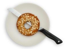 One Whole Grain Bagel on a White plate, isolated on white background. The Bagel is half cut with a knife that has a black handle. Saved with clipping path.
