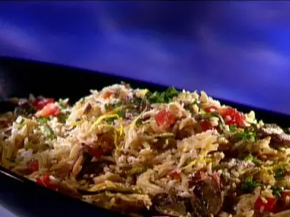 A close up of a serving dish full of garden pilaf. This was made with basmati rice, orzo pasta, shredded zucchini, tomatoes, cremini mushrooms, and parmesan cheese.