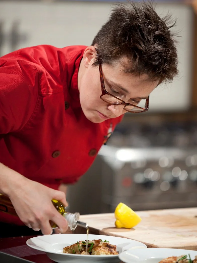 Chef Elise Komack drizzles olive oil over her dish, as seen on Food Network’s Chopped Champions, Season 14.