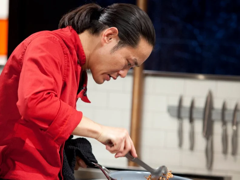 Chef Jun Tanaka stirs ingredients in a pan, as seen on Food Network’s Chopped Champions, Season 14.