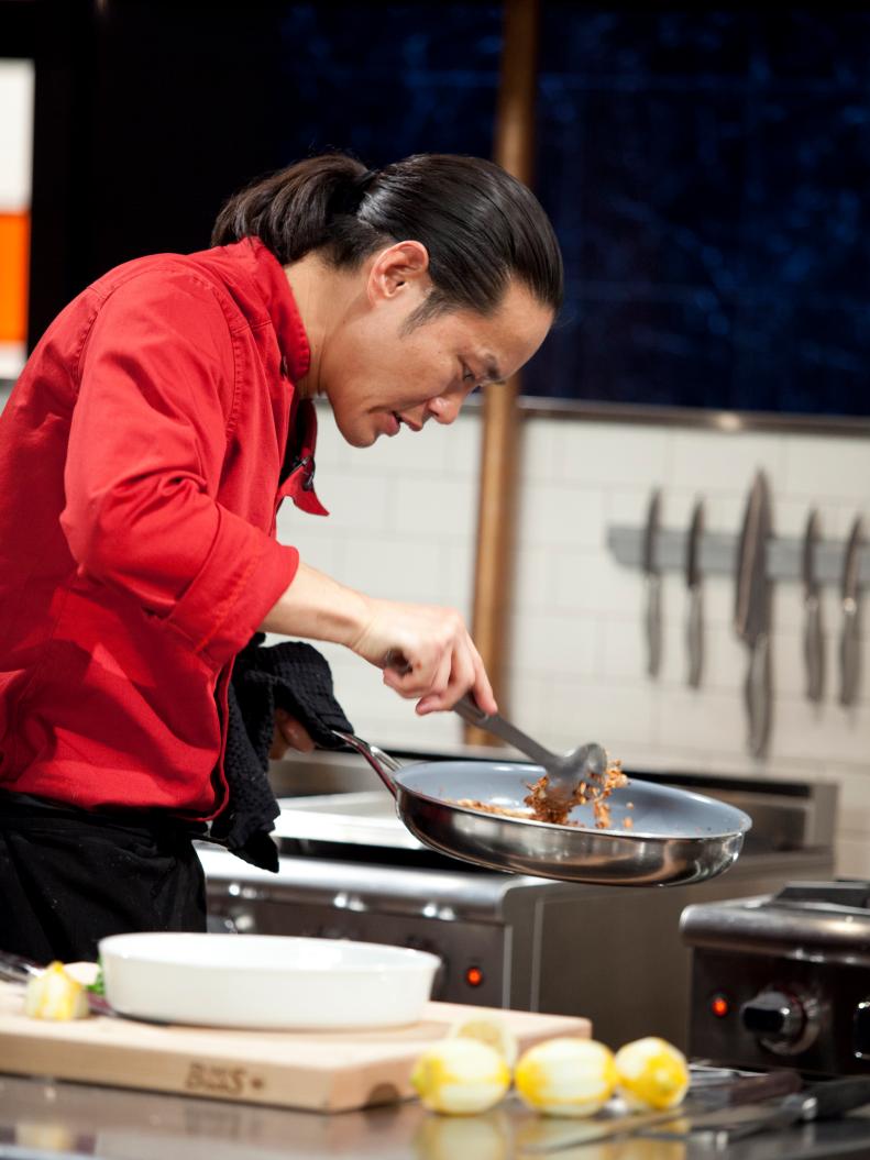 Chef Jun Tanaka stirs ingredients in a pan, as seen on Food Network’s Chopped Champions, Season 14.