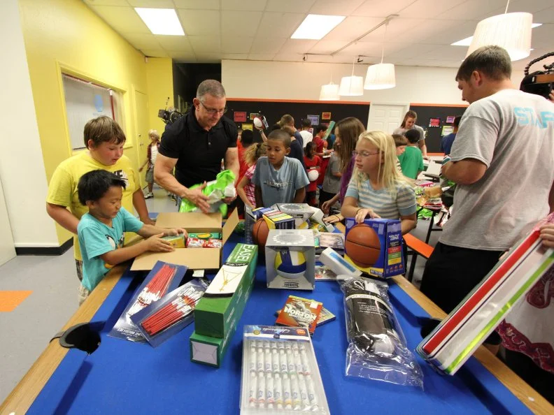 Robert Irvine helps the children at the Boys and Girls club open up all their new toys as seen on Food Network's Restaurant: Impossible Holiday Special, Holiday: Impossible.