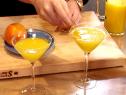 A close up of Bobby Flay's hands as they add orange peel for garnish to his finished sherry cocktails.