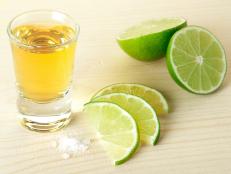 Gold Tequila with lime slices and salt on wood table isolated on white background