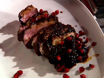 A dish made from seared duck breast that has been cooked in a pomegranate molasses to create a glaze on the outside of the meat. It has been sliced and topped with the sauce and pomegranate seeds.