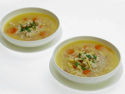 Two shallow white bowls of lemon chicken soup with spaghetti. They have been topped with fresh herbs and grated romano cheese.