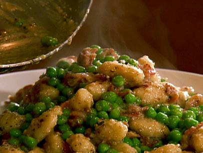 A dish of gnocchi with bacon and sweet peas served in a white bowl.