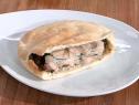 A white plate with a mediterranean pita pocket. It was made with leftover grilled brisket that was placed in a pita pocket with pickled cucumbers and a yogurt mixture.