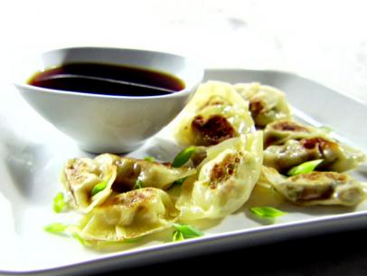 A white plate with chicken potstickers. These were made with wonton wrappers that were filled with leftover chicken teriyaki and fried in a pan with oil. On the plate is a bowl with a vinegar and soy sauce dipping sauce.