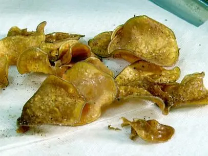 A close up of spicy sweet potato chips sitting on a white paper towel. The chips are made from sweet potatoes that have been fried. The seasoning contains salt, pepper, smoked paprika, ancho chile powder and garlic powder.