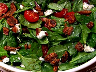 A spinach salad with spiced pecans, cherry tomatoes, blue cheese crumbles, and a dressing made with mustard, vinegar, and oil.