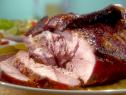 A close up of a pork roast that has been cooked and cut. The roast is sitting on a dark yellow plate. The outside of the roast is a dark brown and dark red from being cooked in an oven. The inside of the roast is light red and white from being cooked.
