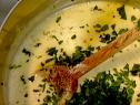 A pot of gorgonzola cheese sauce that has been cooking in a pot. Fresh minced parsley has been added and will be stirred with the wooden spoon.