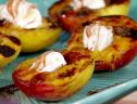 A close up of a grilled peach dessert with creme fraiche in the center and drizzled with wine syrup and honey.