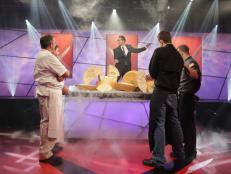 The Chairman, Mark Dacascos unveils the secret ingredient, parmigiano reggiano cheese to Iron Chefs Bryan Forgione, Marc Forgione and Challenger Chefs Joey Campanaro and Lou Campanaro, as seen on Food Network's Iron Chef America, Season 10 episode 1012.  