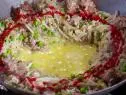 A pan of pork fried dirty rice cooking with hot sauce drizzled on it
