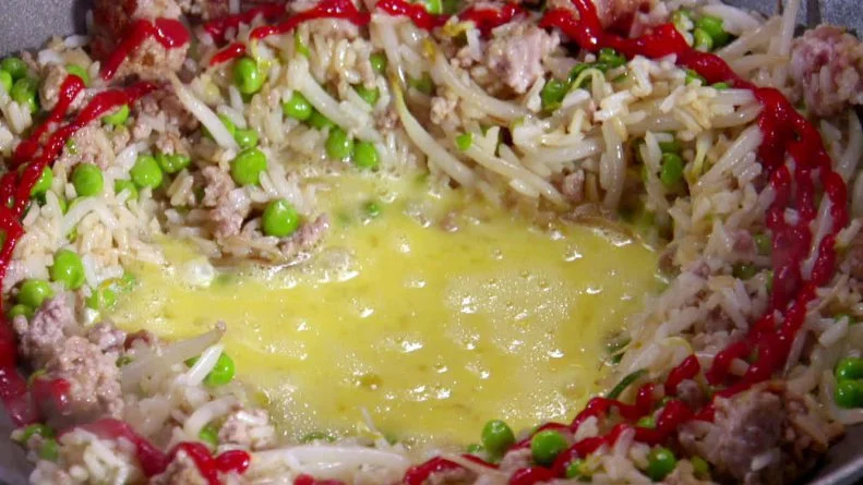 A pan of pork fried dirty rice cooking with hot sauce drizzled on it