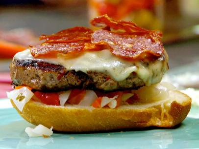 A close up of Rachael Ray's ultimate salami burger with hot pickled vegetable relish, melted provolone cheese, and oven crisped salami.