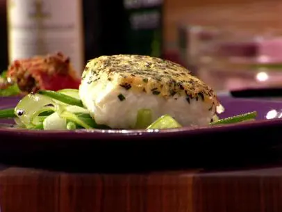 A close up of herb crusted halibut served on top of curly celery and green beans and served on a purple plate.