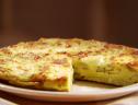 A close up of a zucchini and goat cheese frittata with a slice removed.