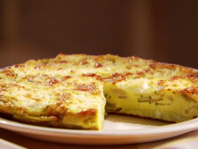 A close up of a zucchini and goat cheese frittata with a slice removed.