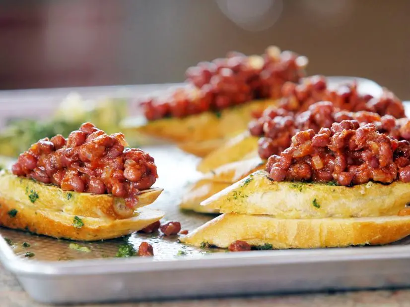 Roger Mooking prepares his BBQ Baked Beans with Cilantro Pesto on Cheesy Texas Cut Toast as he and Elizabeth Karmel cook at the Michelson home in Lockhart, TX, as seen on Cooking Channel's Red, White, and Grill special featuring Williams-Sonoma.