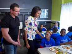 Restaurant: Impossible's host Robert Irvine is on a special assignment for The First Lady, Michelle Obama. His mission is to help out Horton's Kids, a Washington, D.C. organization that educates and empowers children. He is tasked with remodeling the community center where the kids have their meals and creating a community garden so the children can learn about growing food and healthy eating. Shown in this photo, from left, host Robert Irvine and special guest First Lady Michelle Obama talk with children from Horton's Kids in their new dining area as seen on Food Network's Restaurant: Impossible, Season 3.