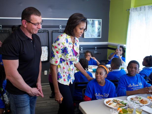 Restaurant: Impossible's host Robert Irvine is on a special assignment for The First Lady, Michelle Obama. His mission is to help out Horton's Kids, a Washington, D.C. organization that educates and empowers children. He is tasked with remodeling the community center where the kids have their meals and creating a community garden so the children can learn about growing food and healthy eating. Shown in this photo, from left, host Robert Irvine and special guest First Lady Michelle Obama talk with children from Horton's Kids in their new dining area as seen on Food Network's Restaurant: Impossible, Season 3.