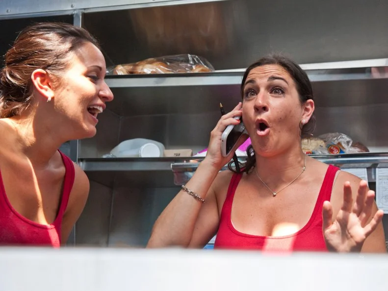 Nonna's Kitchenette's Jaclyn Kolsby takes a phone call as Jessica Stambach looks on in Fayetteville, Ark., as seen on Food Network's The Great Food Tuck Race, Season 3.