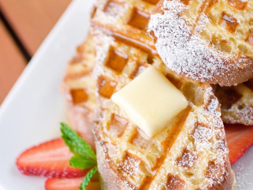 Delicious slices of baguette dipped into a rich egg batter and finished off in a waffle iron.  Served with a melty pat of fresh sweet cream butter, strawberries, maple syrup and confectioner's sugar.  Shallow dof, focus in the front.