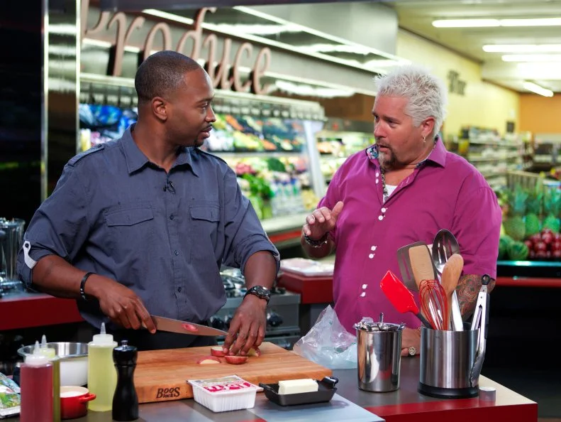 Host Guy Fieri with Chef Stanley Hagerman during the cooking part of Game 2, Budget Battle, Family Meal for 4 with $5.91, as seen on Food Network's Guy's Grocery Games, Season 1.