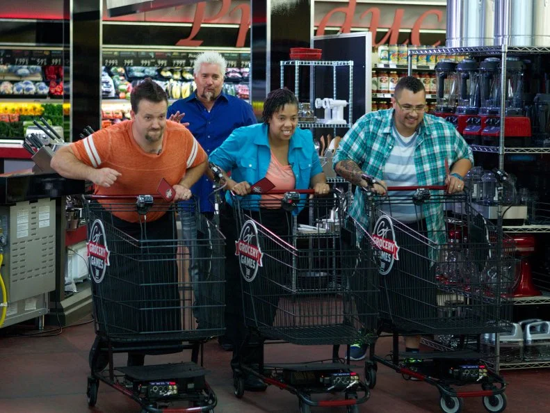 Host Guy Fieri with Chef Kris Plummer, Chef Monica Smith, and Nick Wilson during the start of the shopping portion of Game 2, Grocery List, Fun Family Meals, with Ad Sales Integration featuring Kellogg's Eggo's, Kellogg's Eggo's Homestyle Waffles, as seen on Food Network's Guy's Grocery Games, Season 1.