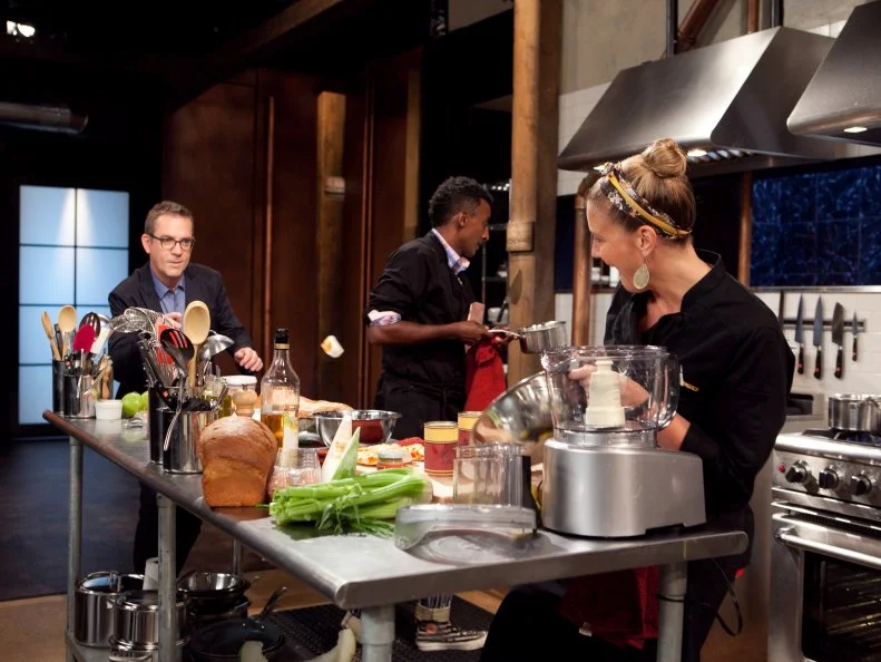 Chopped: After Hours host Ted Allen tries to bounce some of Chef Amanda Freitag's vegan lobster into a mixing bowl off of Chef Marcus Samuelssons works station working, as seen on Food Network's Chopped: After Hours.