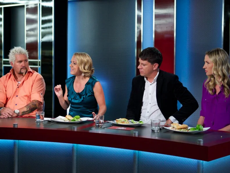 Host Guy Fieri with judges Melissa D'Arabian, Troy Johnson, and Catherine McCord during the judging of Game 3, Bag Swap, Gourmet Lunch, 3 min to shop and 30 min cooking time, as seen on Food Network's Guy's Grocery Games, Season 1.