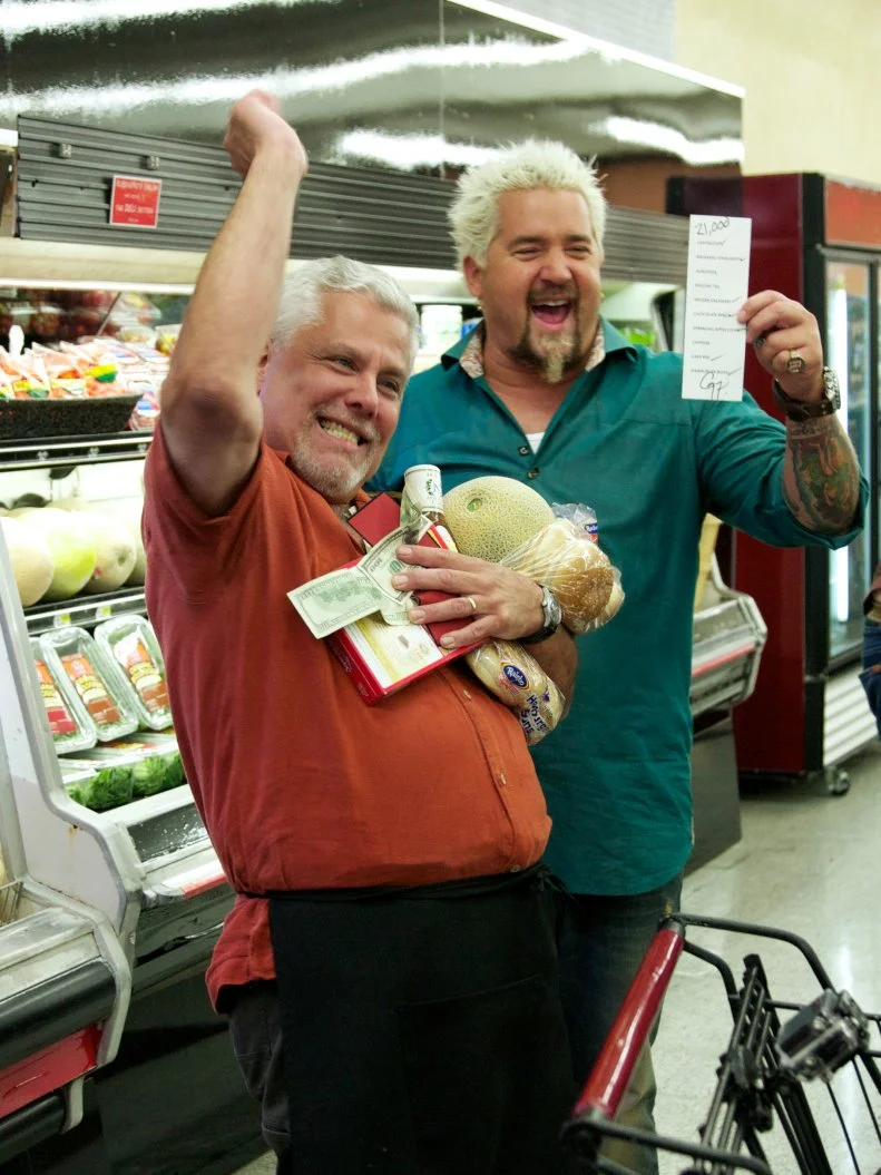 Host Guy Fieri with chef Claude Baltran, winner of $21,000, after the shopping spree with a chance to win $20,000 by grabbing all the items on the grocery list within 2 minutes, as seen on Food Network's Guy's Grocery Games, Season 1.
