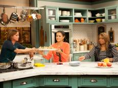 Host Marcela Valladolid has a platter of Pan-Seared Pork Chops with Pineapple Gravy and Mexican Couscous to co-host Katie Lee, as seen on Food Network's The Kitchen, Season 1.