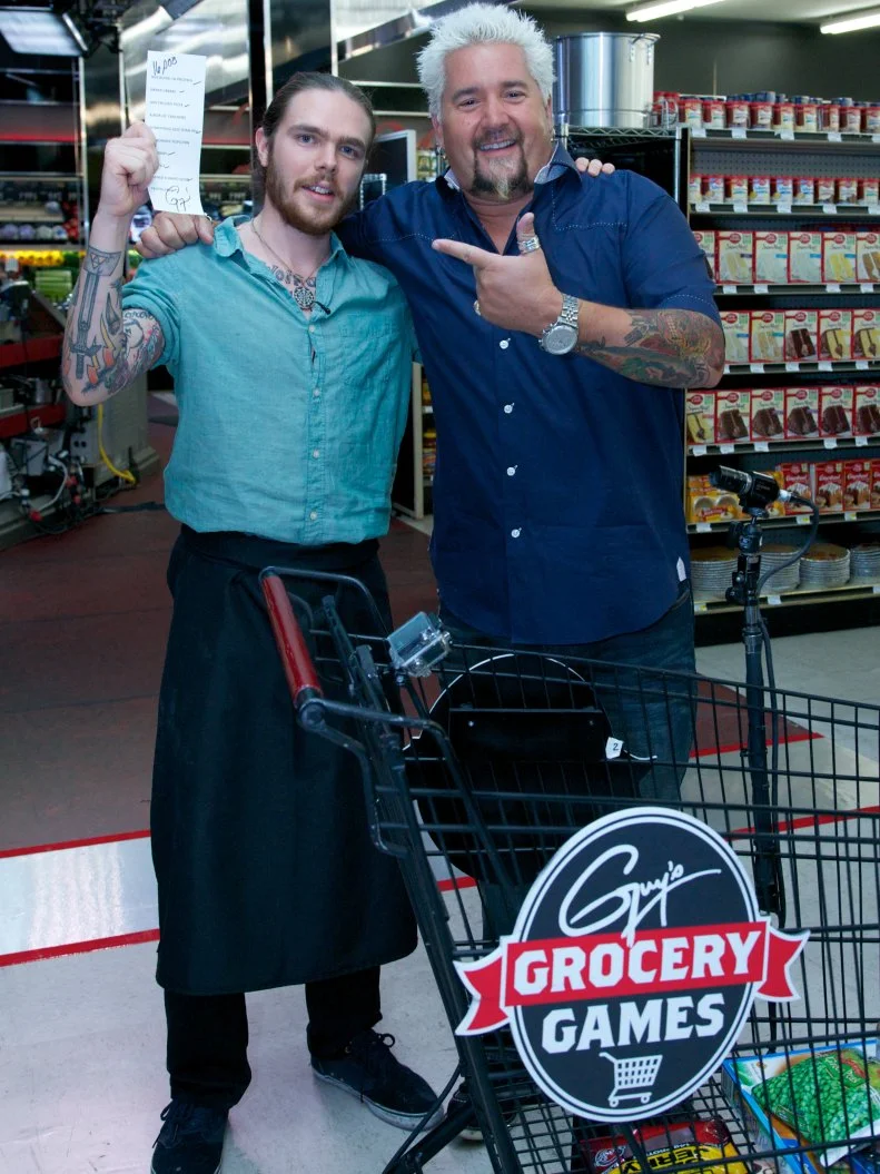 Host Guy Fieri poses with chef Phillip Franklin Lee, winner of Episode 107, Game 3, 5 Ingredients Or Less, Upscale Chicken Dinner, 35 min cooking time, during the end of the shopping spree with a chance to win $20,000 by grabbing all the items on the grocery list within 2 minutes, as seen on Food Network's Guy's Grocery Games, Season 1. Chef Phillip Franklin Lee wins $16,000.
