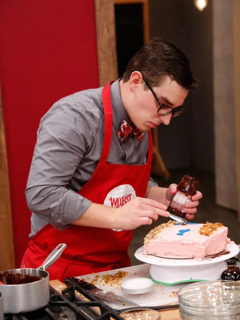 Red Team recruit Michael Haydin preparing his variation of a Basic Vanilla Cake with Swiss Meringue Buttercream Frosting demonstrated by Chef Ron Ben-Israel. Chef Ron gave the recruits very specific directions to follow as a basis for their own unique cakes. Michael is adding Walnuts, Almonds, golded raisins and milk Chocolate between layers to personalize his cake, as seen on Food Network's Worst Cooks in America, Season 4.