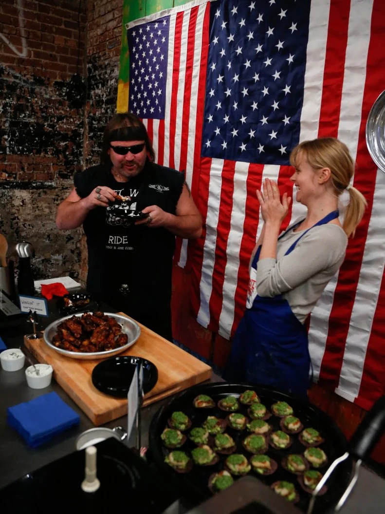 Blue Team Recruit Alina Bolshakova serves the appetizers she made for the "Biker Bites" challenge, and her appetizers seem to be a hit!  Alina made "Wingin' It Chicken Wings" and her assigned second appetizer: Grilled Sea Scallops on Tortilla Chips with Avocado Puree and Jalapeno Pesto. Alina made a spice rub for her chicken wings  flavored with sweet smoked pepper, cayenne pepper, onion and garlic powder, salt and pepper. She then made a glaze with beer, honey, marmalade, hot sauce, jalapeno, lemon juice, orange juice and white grape vinegar. Her dipping sauce was a greek yogurt sauce with cheese, scallions garlic, dill, salt and pepper. The recruits had to prepare their own chicken wing recipe after Chef Bobby Flay demonstrated how to make his Red Chile Chicken Wings with Chipotle Honey Glaze and an additional appetizer for hungry bikers- a tough crowd to please, as seen on Food Network's Worst Cooks in America, Season 4.