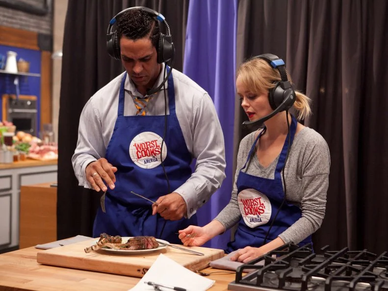 The blue team (Alina Bolshakova and Chet Pourciau) speak to Chef Bobby Flay via headset while they try and describe an unfamiliar dish to the chef that he must replicate by their description alone, as seen on Food Networks Worst Cooks In America, Season 4.